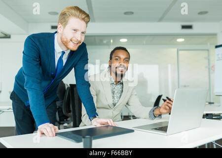 Ein schwarzer junge Mann mit Dreadlocks und ein junger hübscher roten Haaren Geschäftsmann diskutieren Grafiken Designfehler in ein schönes weißes o Stockfoto