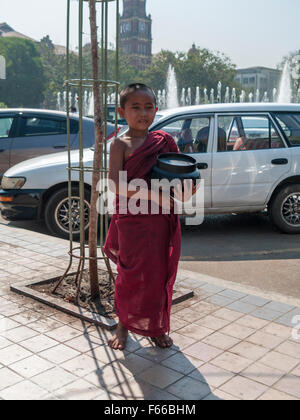 Junge Mönch auf Almsround in der Stadt von Yangon, mit einer Almosenschale. Stockfoto