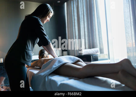 Junge und schöne Massage Therapeuten massieren Client mit wunderschönen Beinen durch die Fenster beleuchtet Stockfoto