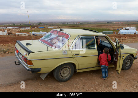 Libanon Beqaa Tal, Deir el Ahmad, Lager für syrische Flüchtlinge, alte deutsche Mercedes Benz 200 D Auto mit alten deutschen country code Kennzeichen D, libanesische Flagge und Bild von Baalbek Tempel, Hintergrund Anti Gebirge Libanon und Syrien Stockfoto