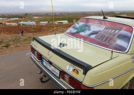 Libanon Beqaa Tal, Deir el Ahmad, Lager für syrische Flüchtlinge, alte deutsche Mercedes Benz 200 D Auto mit alten deutschen country code Kennzeichen D, libanesische Flagge und Bild von Baalbek Tempel, Hintergrund Anti Gebirge Libanon und Syrien Stockfoto