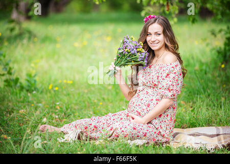 Schöne schwangere Frau mit Blumen im Freien im Sommerpark Stockfoto