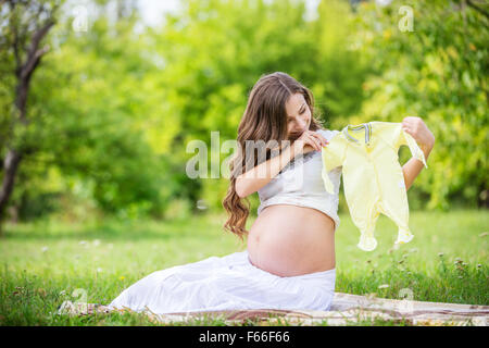 Schöne schwangere Frau hält Babybody und lächelnd draußen im park Stockfoto