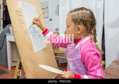 Fünfjähriges Mädchen mit einem Pinsel malt ein Bild auf einer Staffelei und hält in seiner anderen Hand in die Künstler-palette Stockfoto