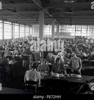 1950er Jahre historische Bild zeigt eine große Gruppe von Fabrikarbeitern in der Kantine zu Mittag. Stockfoto