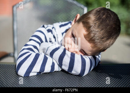 Preteen Boy sitzt am Tisch Kopf ruht auf seinen Armen Stockfoto