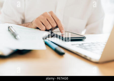 Hautnah auf der Seite eines jungen Geschäftsmann mit Smartphone stützte sich auf eine Laptop - arbeiten, Multitasking, Technologie-Konzept Stockfoto