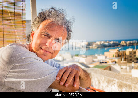 Lächelnd und gebräunte Mann mittleren Alters kaukasischen erholsamen Urlaub, seine Arme vor das atemberaubende Panorama auf eine italienische Küstenstadt überqueren Stockfoto