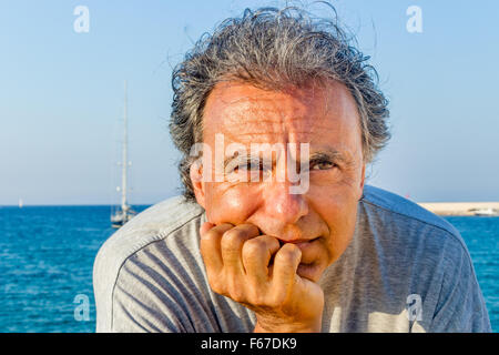 Lächelnd und gebräunte Mann mittleren Alters kaukasischen erholsamen Urlaub, hält sein Kinn vor das atemberaubende Panorama auf eine italienische Küstenstadt Stockfoto