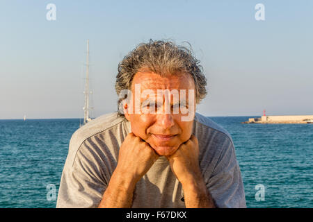 Lächelnd und gebräunte Mann mittleren Alters kaukasischen erholsamen Urlaub, hält sein Kinn vor das atemberaubende Panorama auf eine italienische Küstenstadt Stockfoto