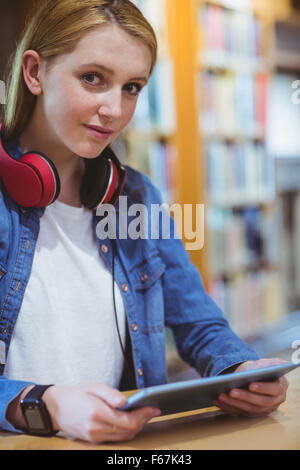 Hübsche Studentin mit Kopfhörern mit Tablet in Bibliothek Stockfoto