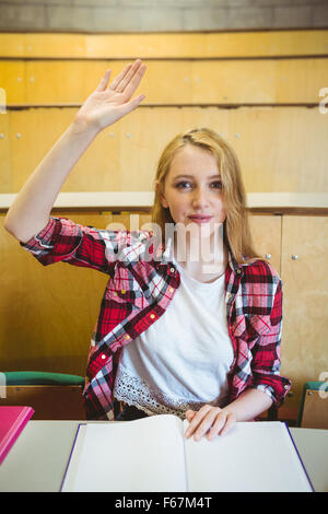 Blonde Studentin, die Hand heben, während des Unterrichts Stockfoto