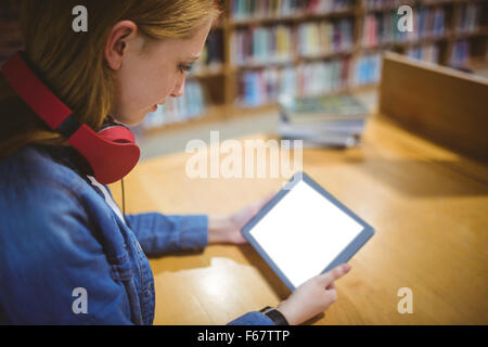 Hübsche Studentin mit Kopfhörern mit Tablet in Bibliothek Stockfoto