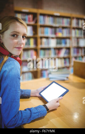 Hübsche Studentin mit Kopfhörern mit Tablet in Bibliothek Stockfoto