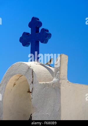 Ein blaues Kreuz und ein Spatz auf eine weiß getünchte Kirche in Santorini Griechenland Stockfoto