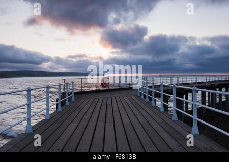 Blick entlang Whitbys West Pier bei Sonnenuntergang - dramatische Wolken am Himmel über den Holzsteg blau-grau und das Meer. Yorkshire Coast, England, GB, UK. Stockfoto