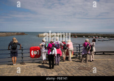 Rückansicht der Gruppe von Reifen Freundinnen stehend, mit Blick auf den malerischen Hafen, Staithes, Yorkshire, England an sonnigen Sommertag mit blauem Himmel. Stockfoto