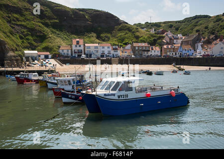 An einem sonnigen Sommertag sind Angelboote/Fischerboote und Cobles nebeneinander im Hafen - Küste Dorf Staithes, North Yorkshire, England, UK festgemacht. Stockfoto