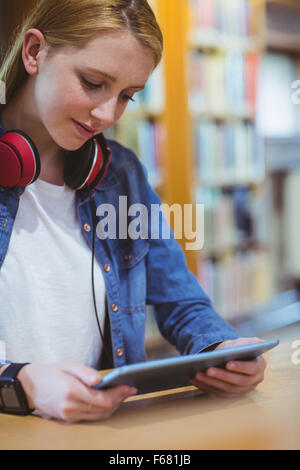 Hübsche Studentin mit Kopfhörern mit Tablet in Bibliothek Stockfoto
