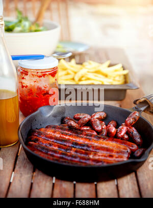 Lecker gebratene Bratwurst vom Grill, Pommes Frites und Sauce auf den Tisch, Grill-Picknick im grünen, leckeres Essen Stockfoto