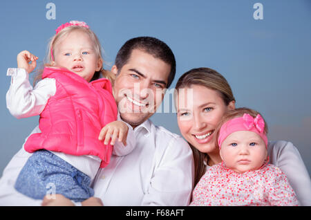 Porträt der glücklichen Familie stehend auf blauen Himmelshintergrund, Eltern mit zwei entzückende Töchter Spaß im freien Stockfoto