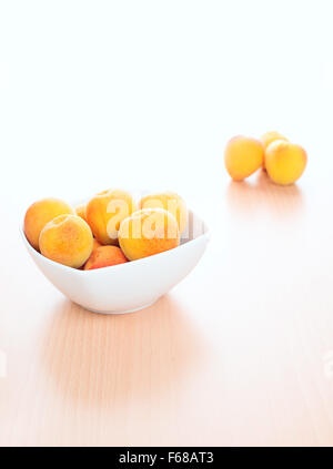 Frische Aprikosen, weiße Schüssel auf Küche Holztisch Hintergrund Stockfoto