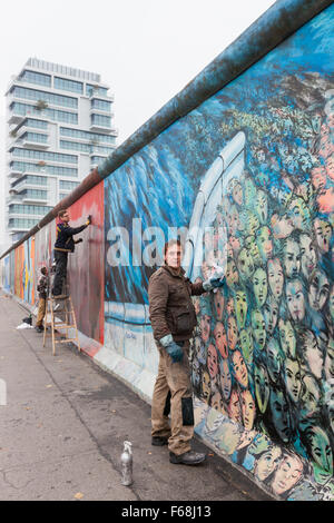 BERLIN, Deutschland - 30. Oktober 2015: Ein Mann reinigt Graffiti aus ein Wandbild an der East Side Gallery. Das Kunstwerk "Es geschah In N Stockfoto