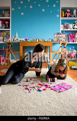 Vertikale portrait ein kleines Mädchen und ihre Mutter spielen mit traditionellen Kunststoff Steine in ein Spielzimmer. Stockfoto