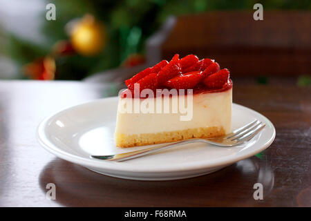 Frische Erdbeer Käsekuchen. Selektiven Fokus an der oberen Vorderkante des Kuchens. Weihnachtsbaum im Hintergrund Stockfoto