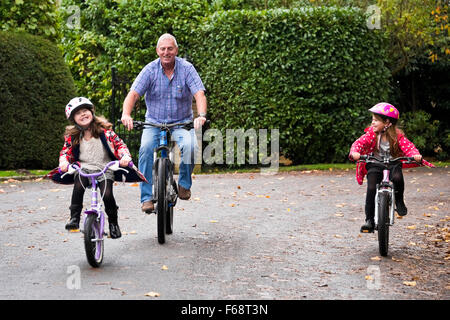 Horizontale Porträt der jungen Mädchen, die ihre Fahrradfahren entlang der Straße mit ihrem Opa. Stockfoto