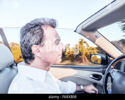 Seitenansicht des gut aussehend Mann mittleren Alters mit Salz Pfeffer Haare und trägt ein weißes Hemd, während er ein Cabrio auf dem Lande fährt Stockfoto