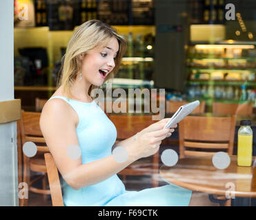 junge Frau sitzt in einem Café auf der Suche sehr überrascht bei der Zeitung Stockfoto