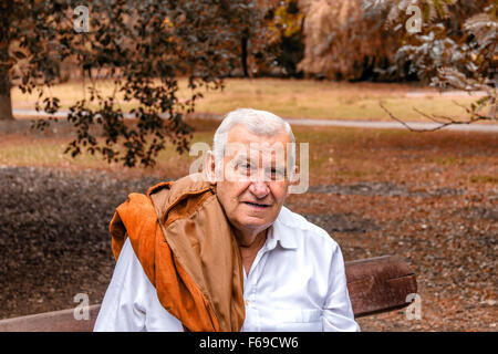 Senior mit Wildlederjacke über Schulter und weißen Hemd in einem grünen park Stockfoto