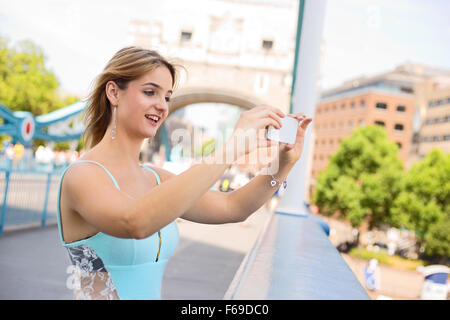 junge Frau, die ein Foto von der Tower Bridge mit ihrem Telefon Stockfoto