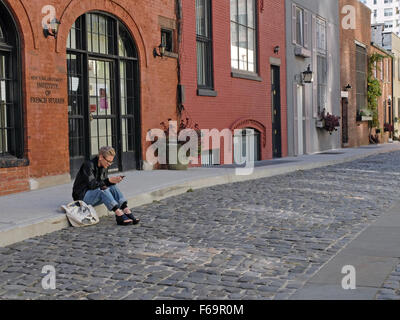 Eine Frau liest aus ihrem Handy auf Washington Mews, gated eine Private Street in Greenwich Village, Manhattan, New York City Stockfoto