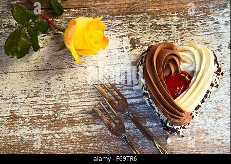 Stillleben mit herzförmigen Kuchen, zwei Gebäck Gabeln und eine gelbe rose Stockfoto