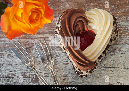 Stillleben mit herzförmigen Kuchen, zwei verzierten Kuchen Gabeln und eine orange rose Stockfoto