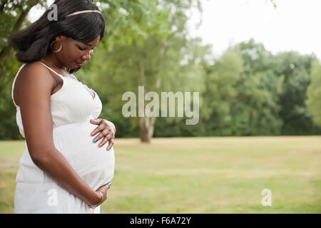 Schwangere Afrikanerin in der Natur mit weißen Kleid Stockfoto