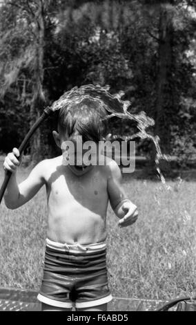 Eine Momentaufnahme einer Person, die sich an einem warmen Tag mit einem Gartenschlauch in Tallahassee, Florida, abkühlt. Die Szene spiegelt typische Sommeraktivitäten wider, wobei die Person einen erfrischenden Moment in der Hitze im Freien genießt und den Alltag in einer floridischen Stadt veranschaulicht. Stockfoto