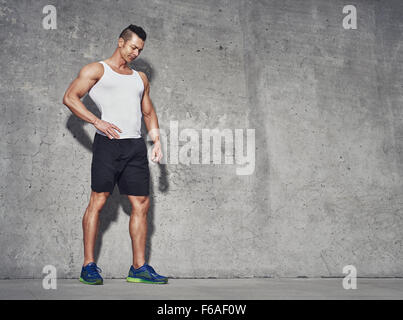 Männlichen Fitness-Modell in weißen Tank-Top Entspannung nach dem Training. Grauer Hintergrund mit Platz für Text, Textfreiraum