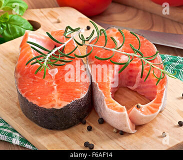 Frisch und roh Steaks Forelle auf einem Holzbrett mit in Scheiben geschnittenen Zitrone, Rosmarin und Pfeffer Stockfoto