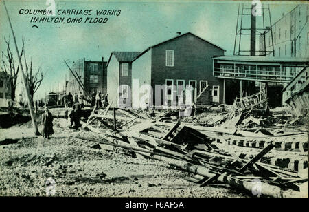 Die Columbia Carriage Works in Hamilton, Ohio, ist auf einer historischen Postkarte dargestellt, die die Schäden durch eine Überschwemmung zeigt. Dieses Bild zeigt die Auswirkungen industrieller Überschwemmungen auf lokale Einrichtungen und die Herausforderungen, denen sich die Gemeinde und die Unternehmen bei solchen Katastrophen gegenübersehen. Stockfoto