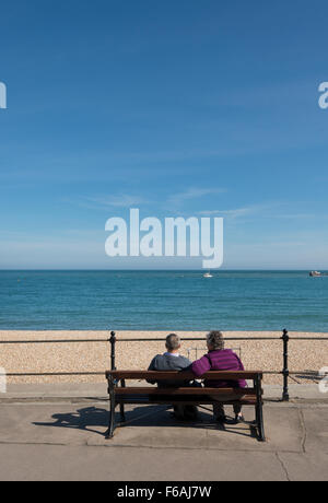 Mittleren gealterten paar sitzt auf Holzbank auf Lyme Regis direkt am Meer mit Blick auf das Meer Stockfoto