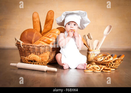 Kleine Köchin. Kleines Kind in eine Kochmütze mit Weidenkörbe von Gebäck, Brötchen, Brot und Brötchen Stockfoto