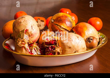 Schale mit Granatäpfeln auf einem Holztisch mit Mandarinen auf dem Hintergrund gesetzt Stockfoto