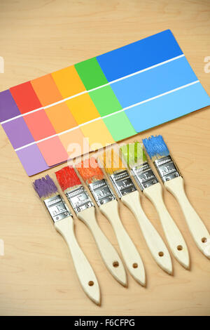 Pinsel mit verschiedenen Farben mit Farbproben auf Holztisch Stockfoto