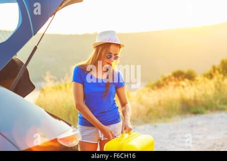 Eine junge Frau mit einem gelben Koffer stehen in der Nähe der Kofferraum eines Autos am Straßenrand geparkt Stockfoto