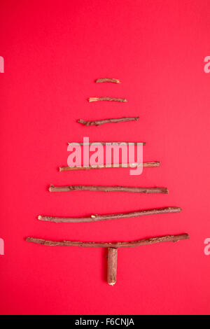 Weihnachtsbaum aus Stöcken auf rotem Hintergrund angeordnet Stockfoto