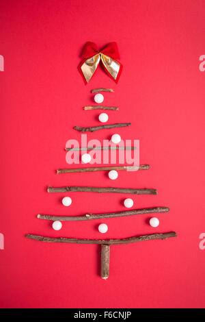 Weihnachtsbaum aus Stöcken und weiße Kugel auf rotem Hintergrund angeordnet Stockfoto