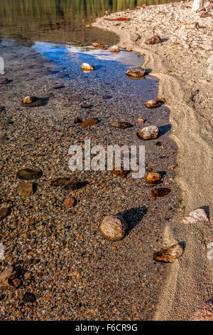 Mehrere größere Felsen sitzen im flachen Wasser neben dem Ufer. Stockfoto